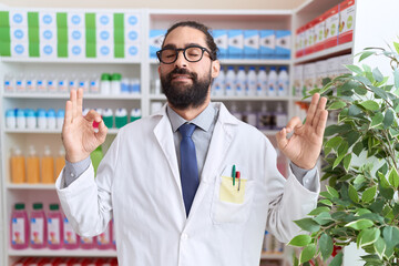 Hispanic man with beard working at pharmacy drugstore relax and smiling with eyes closed doing...