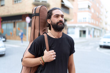 Young hispanic man musician holding guitar case at street