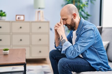 Young bald man stressed sitting on sofa at home