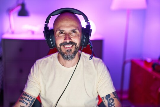 Young bald man streamer smiling confident sitting on table at gaming room