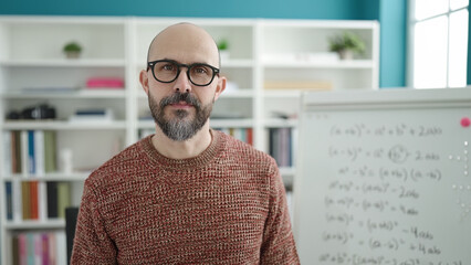 Young bald man teacher standing with relaxed expression at university classroom