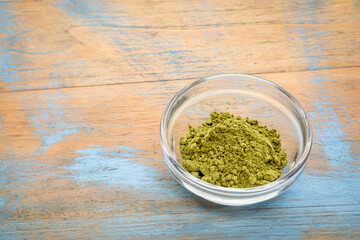 organic matcha green tea powder in a small glass bowl against grunge wood