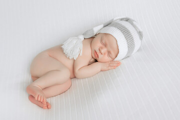 Newborn boy in a knitted cap sleeps on white cloth. Newborn boy sleeps sweetly in the first days of life. 