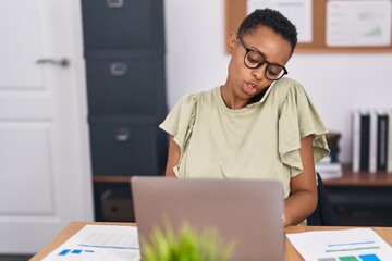 African american woman business worker using laptop talking on smartphone at office