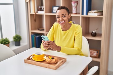 Fototapeta na wymiar African american woman having breakfast using smartphone at home