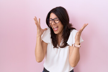 Middle age hispanic woman wearing casual white t shirt and glasses celebrating mad and crazy for...