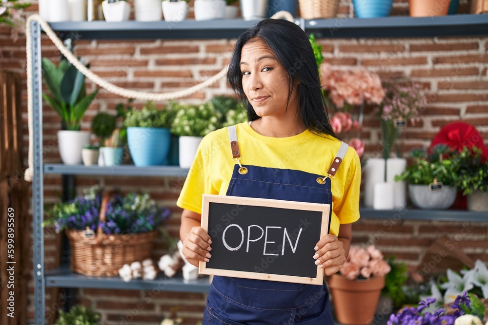 Wall mural hispanic woman working at florist holding open sign smiling looking to the side and staring away thi