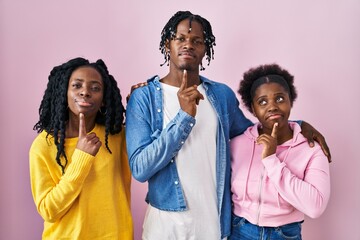 Group of three young black people standing together over pink background thinking concentrated about doubt with finger on chin and looking up wondering