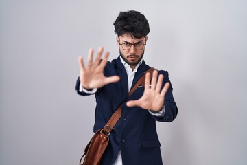 Hispanic man with beard wearing business clothes afraid and terrified with fear expression stop gesture with hands, shouting in shock. panic concept.