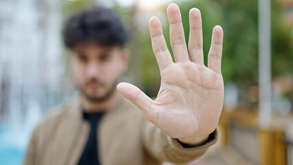 Young hispanic man doing stop gesture with hand at park