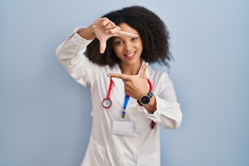 Young african american woman wearing doctor uniform and stethoscope smiling making frame with hands and fingers with happy face. creativity and photography concept.