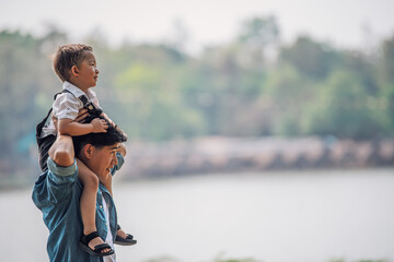 young asian father carrying son on back having fun enjoying nature outdoors in park