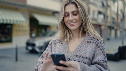 Young blonde woman smiling confident using smartphone at street