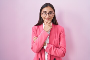 Young hispanic woman wearing business clothes and glasses looking confident at the camera smiling with crossed arms and hand raised on chin. thinking positive.