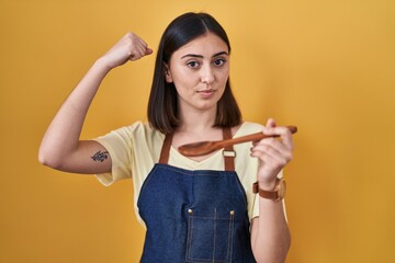 Hispanic girl eating healthy  wooden spoon strong person showing arm muscle, confident and proud of power