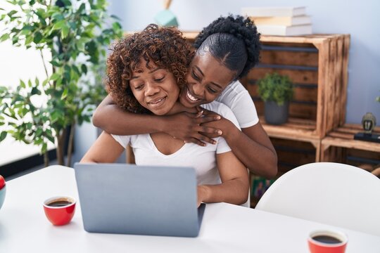 African american women mother and daughter hugging each other using laptop at home