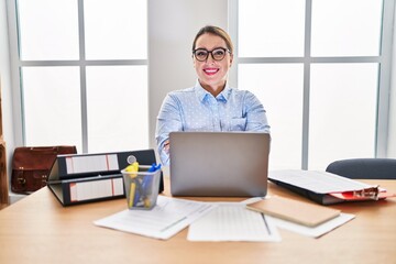 Fototapeta na wymiar Young hispanic woman working at the office wearing glasses happy face smiling with crossed arms looking at the camera. positive person.