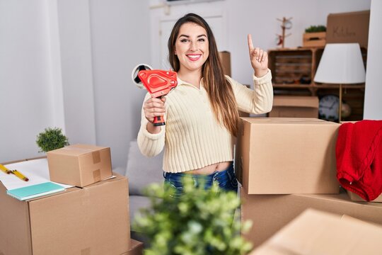 Young hispanic woman moving to a new home packing boxes surprised with an idea or question pointing finger with happy face, number one