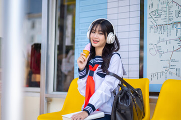 Portrait of a happy japanese school girl listening to music via headphones at ice cream shop,...