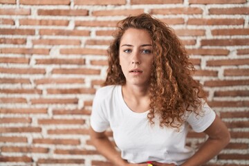 Young caucasian woman standing over bricks wall background with hand on stomach because indigestion, painful illness feeling unwell. ache concept.