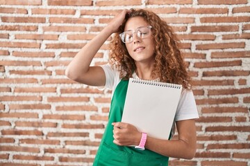 Young caucasian woman holding art notebook smiling confident touching hair with hand up gesture, posing attractive and fashionable