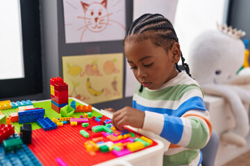 African american boy playing with construction blocks sitting on table at kindergarten