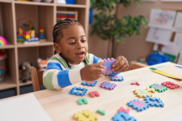 African american boy playing with vocabulary puzzle game sitting on table at kindergarten