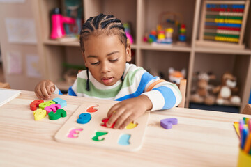 African american boy playing with maths puzzle game sitting on table at kindergarten