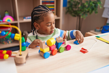 African american boy playing with blocks train toy sitting on table at kindergarten