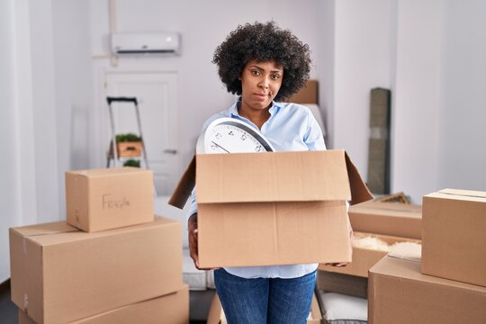 Black woman with curly hair moving to a new home holding cardboard box depressed and worry for distress, crying angry and afraid. sad expression.