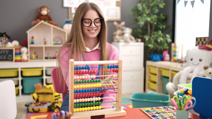 Young blonde woman preschool teacher teaching maths with abacus at kindergarten