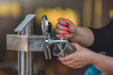 The bartender pours craft beer from the tap into a glass. The hand at the beer tap pours draft beer...