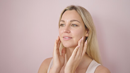 Obraz na płótnie Canvas Young blonde woman smiling confident touching face over isolated pink background