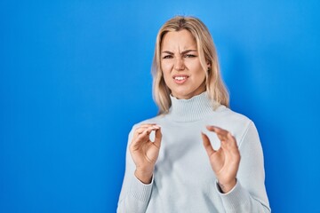Young caucasian woman standing over blue background disgusted expression, displeased and fearful...