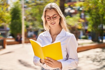 Young blonde woman smiling confident reading book at park