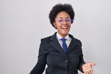 Beautiful african woman with curly hair wearing business jacket and glasses smiling cheerful with open arms as friendly welcome, positive and confident greetings