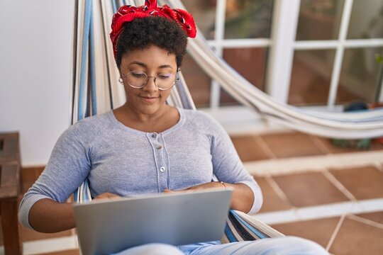 African american woman using laptop lying on hammock at home terrace