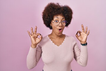 Young african american woman standing over pink background looking surprised and shocked doing ok approval symbol with fingers. crazy expression
