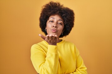 Obraz na płótnie Canvas Young african american woman standing over yellow background looking at the camera blowing a kiss with hand on air being lovely and sexy. love expression.