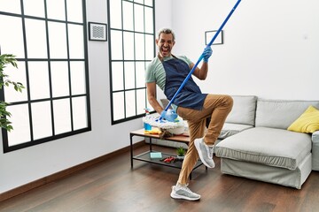 Middle age grey-haired man using mop as a guitar at home