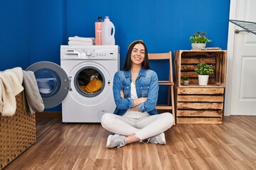 Hispanic woman doing laundry sitting on the floor happy face smiling with crossed arms looking at...