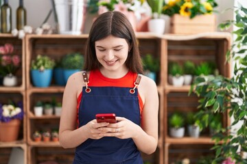 Young caucasian woman florist smiling confident using smartphone at florist