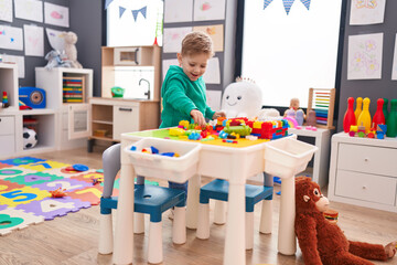 Adorable caucasian boy playing with construction blocks standing at kindergarten