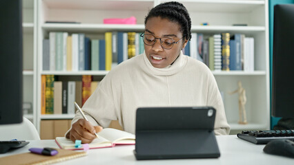 African american woman student using touchpad writing notes at library university