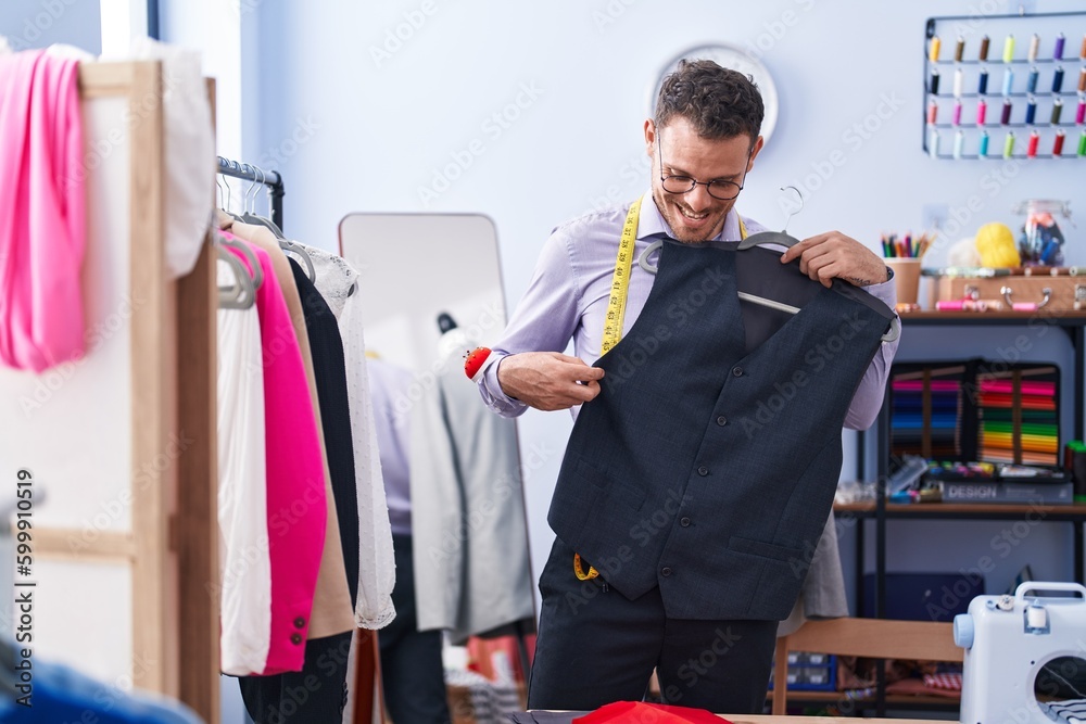 Wall mural young hispanic man tailor smiling confident holding waistcoat at tailor shop