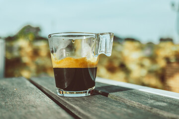 A glass of espresso sits on a table in front of a blurred background.