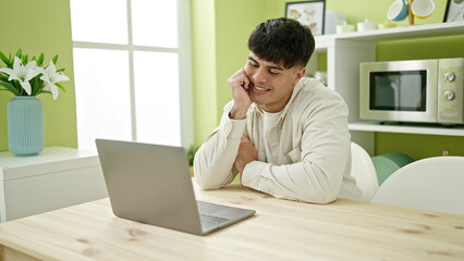 Young hispanic man having video call sitting on table at dinning room