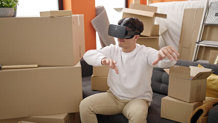 Young hispanic man wearing virtual reality glasses sitting on the sofa at new home
