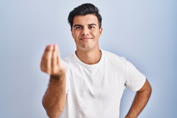 Obraz premium Hispanic man standing over blue background doing italian gesture with hand and fingers confident expression