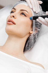 Professional dermatologist in medical gloves doing hydro peeling procedure for beautiful woman patient in cosmetology clinic. Close up facial treatment.